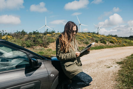 A tourist girl next to the car looks at the map of the area for further travel.