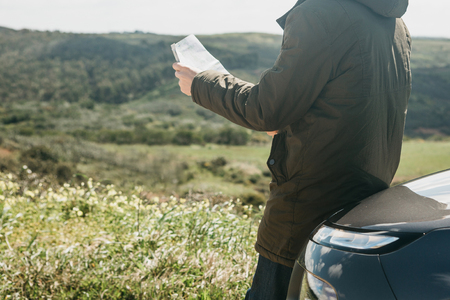 A tourist man next to the car looks at the map of the area for further travel.