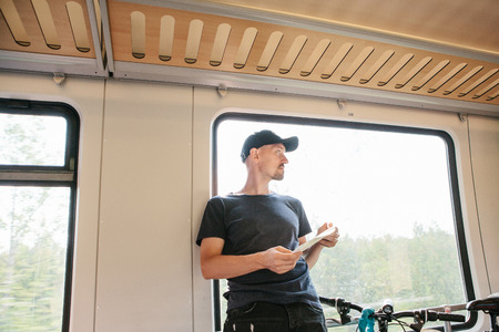 Tourist in a baseball cap in casual clothes by the window in the train with a map in hand. Train...