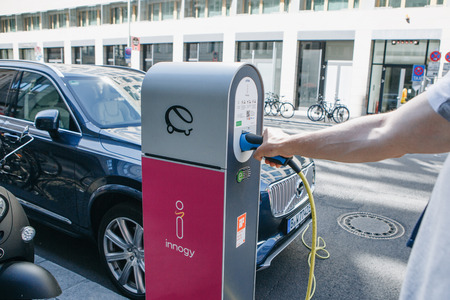 Berlin, August 29, 2018: Street electric filling station for electric car refueling. Eco-friendly mode of transport. A person inserts a cord or cable to charge a car.のeditorial素材
