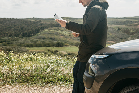 A tourist man next to the car looks at the map of the area for further travel.