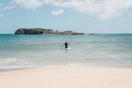 A young woman surfer swims into the sea or ocean to start surfing.