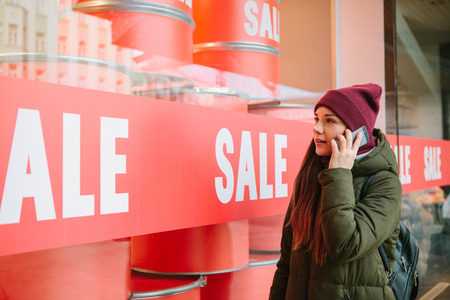 The girl calls on the phone and talks about interesting products that she saw at the sale. Time of off-season and winter sales, Black Friday and Cyber Monday.の写真素材