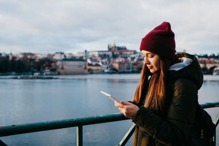 A tourist girl on the street in Prague at sunset uses a tablet in order to view the map or the Internet or use a mobile application.の写真素材