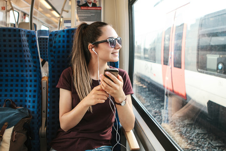 A young girl listens to a music or podcast while traveling in a train.の写真素材