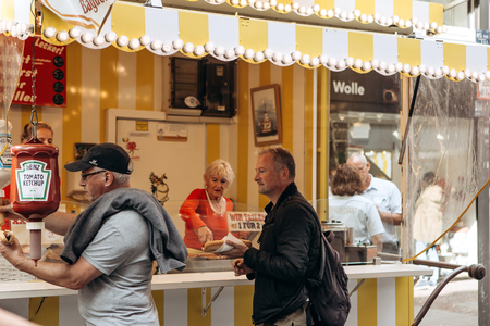 Germany, Muenster, October 5 2018: Street tent selling fried sausage. One customer pours tomato sauce, another waits. Small business at the city fair.のeditorial素材