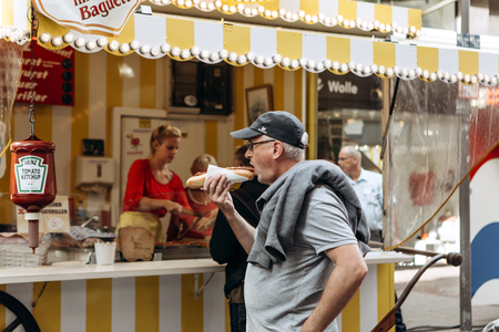 Germany, Muenster, October 5 2018: Street tent selling fried sausage. A man eats fried sausage with a sauce in a fresh baguette. Small business at the city fair.のeditorial素材
