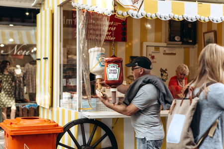 Germany, Muenster, October 5 2018: Street tent selling fried sausage. Buyer pours tomato sauce. Small business at the city fair.のeditorial素材