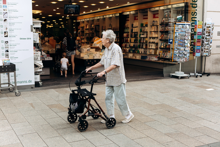 Germany, Leipzig, October 6, 2018: An elderly woman with a special cart for the elderly is walking down the street.のeditorial素材
