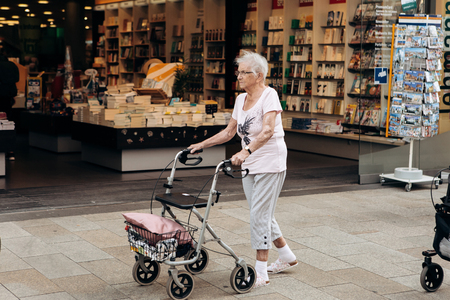 Germany, Leipzig, October 6, 2018: An elderly woman with a special cart for the elderly is walking down the street.のeditorial素材