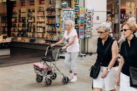 Germany, Leipzig, October 6, 2018: An elderly woman with a special cart for the elderly is walking down the street.のeditorial素材