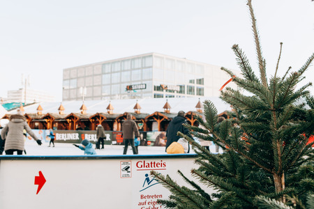 Berlin, December 25, 2017: People ride on an open skating rink on Alexanderplatz in Berlin in Germany during the Christmas holidays. Sports and fun pastime. Focus on the Christmas tree in the foreground.のeditorial素材