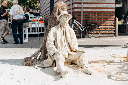 Germany, Muenster, October 5, 2018: A street artist performs living statue covered with dried mud, as if it were in a desert.のeditorial素材