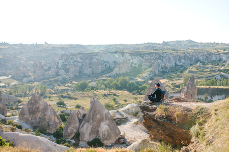A man with a backpack or a tourist sits on top of a hill in Cappadocia in Turkey and meditates or seeks the soul or spends time in solitude.の写真素材