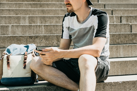 A tourist or student sits on the stairs, rests and uses a mobile phone.の写真素材