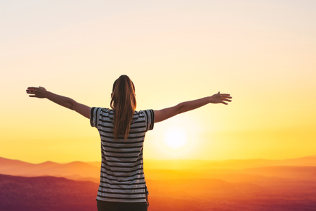 The girl admires a beautiful view of the sunrise or sunset and raises her hands up.の写真素材
