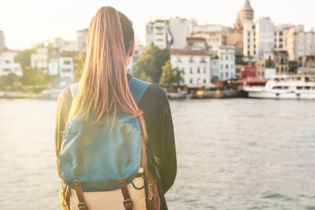 Young tourist girl with a backpack at sunset next to the Bosphorus on the background of Istanbul.
