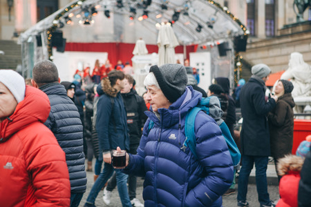A lot of people at the Christmas market in Berlin during the Christmas holidays. In the foreground, an elderly woman drinks hot tea to keep warm.のeditorial素材