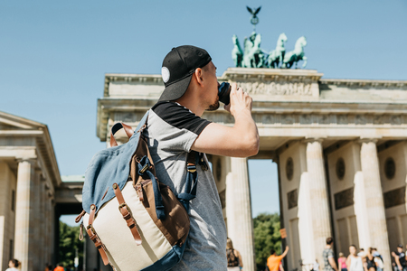 A person drinks from a disposable cup of coffee or another drink during a walk or sightseeing in Berlin in Germany. Ahead is the Brandenburg Gate and blurred unrecognizable people.の写真素材