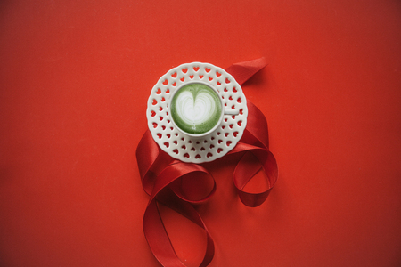 Delicious fresh green matcha coffee with a heart pattern on a red background with ribbon. Concept for Valentines Day or Womens Day in a minimal style.の写真素材