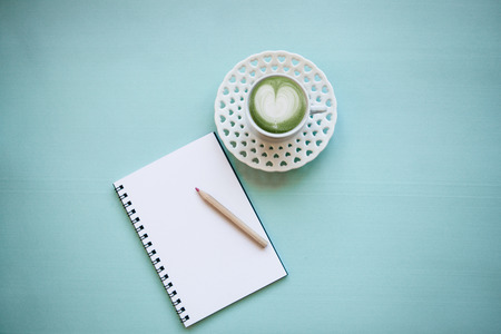 Fresh green Matcha coffee with a heart pattern on a blue background. Near empty diary to write.の写真素材
