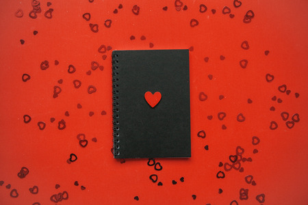 Festive background with many hearts for Valentines Day or another holiday or love event. In the center is a black notebook with a red heart.の写真素材