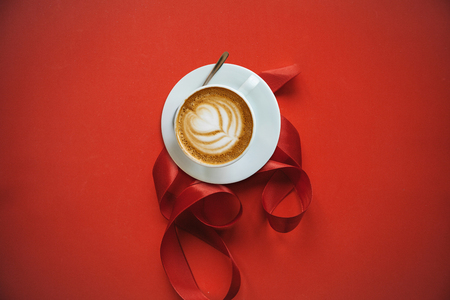 A cup with a traditional tasty and aromatic morning cappuccino on a red background with tape.の写真素材