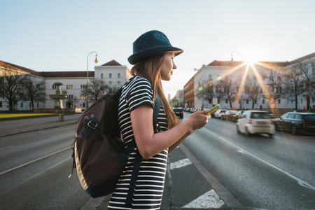 A tourist girl or student with a backpack walks along a street in Munich in Germany and uses a mobile phone.の写真素材