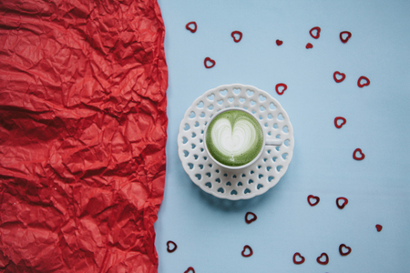 A cup with a tasty and aromatic morning matcha latte coffee on a festive background with many hearts. Next to a red background there is a place for text. Celebration of Valentines Day or Womens Day or other love event.の写真素材