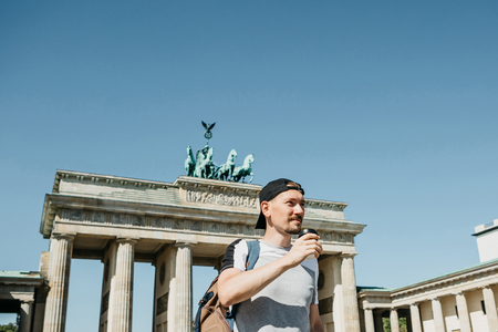 A person drinks from a disposable cup of coffee or another drink during a walk or sightseeing in Berlin in Germany. Ahead is the Brandenburg Gate.の写真素材