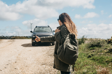 Girl tourist with a backpack travels hitchhiking. She raised her finger up and tried to stop the car to continue her journey.の写真素材