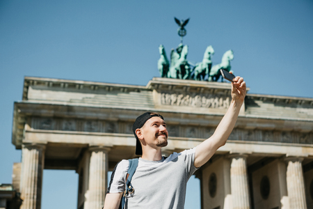 Tourist guy taking a selfie on the background of the Brandenburg Gate in Berlin in Germany or taking pictures of sightsの写真素材
