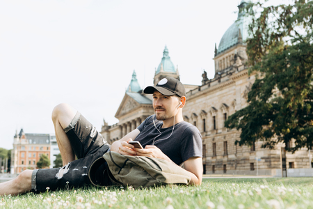 A young guy with a backpack or a student lies on the grass and listens to music or a podcast and enjoys.の写真素材