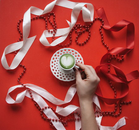 A girl holds in her hand a cup with fresh green Matcha coffee on a holiday background. Concept for Valentines Day or Womens Day.の写真素材