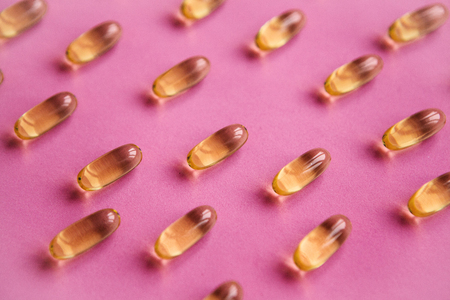 Many transparent pills Omega 3 or fish oil on a pink background.の写真素材