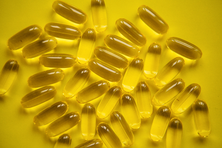 Many transparent pills Omega 3 or fish oil on a yellow background.の写真素材