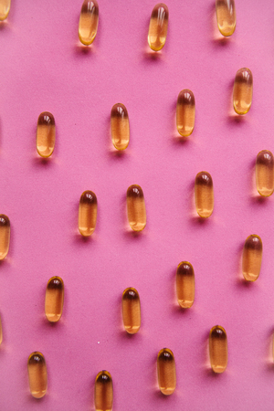 Many transparent pills Omega 3 or fish oil on a pink background.の写真素材