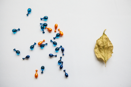 Many pills or capsules with hyaluronic acid and q10 or coenzyme. Caring for skin health. Conceptually, the autumn leaf means aging of the skin, and the capsules with the medicine mean anti-aging.の写真素材