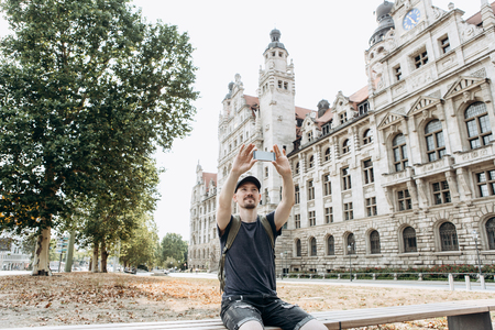 A young man or tourist or student uses a mobile phone to take a photo of a landmark in Leipzig in Germany, or to communicate via video or take a selfie or something else.の写真素材