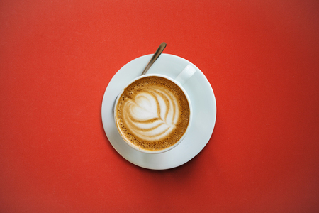 A cup with a traditional tasty and aromatic morning cappuccino on a red background.の写真素材