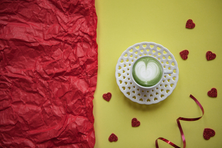 A cup with a tasty and aromatic morning matcha latte coffee on a festive background with many hearts. Next to a red background there is a place for text. Celebration of Valentines Day or Womens Day or other love event.の写真素材