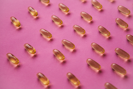 Many transparent pills Omega 3 or fish oil on a pink background.の写真素材