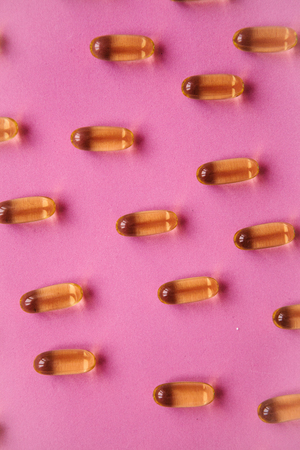 Many transparent pills Omega 3 or fish oil on a pink background.の写真素材