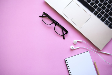Workspace in a trendy pink color. Many different items including a laptop, glasses, notebook, and headphones are on the table. There is a place for text.の写真素材