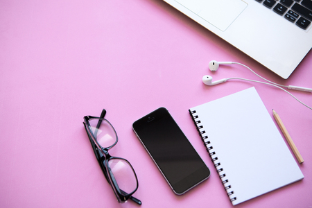 Workspace in a trendy pink color. Many different things including a laptop, headphones, cell phone and notebook are on the table. Nearby there is a place for text.の写真素材