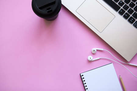 Workspace in a trendy pink color. Many different things including a laptop, notebook and headphones are on the table. Nearby there is a place for text.の写真素材