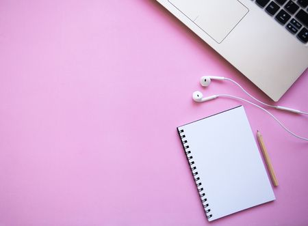 Workspace in a trendy pink color. Many different things including a laptop, notebook and headphones are on the table. Nearby there is a place for text.の写真素材