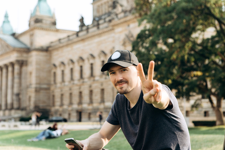 Young man tourist or student sitting on the grass in the streets of Leipzig in Germany and shows the hand gesture means peace.の写真素材
