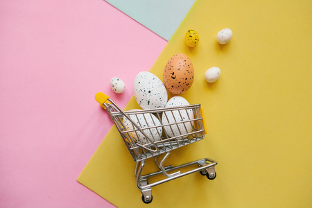 Shopping Cart with eggs on a multi-colored background. The concept of a festive Easter sale in a minimal style.の写真素材