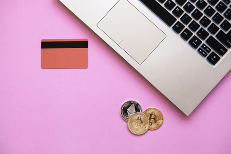 Conceptual photo of e-commerce with credit cards and cryptocurrency. Computer, cryptocurrency and credit card on a trendy pink background.の写真素材
